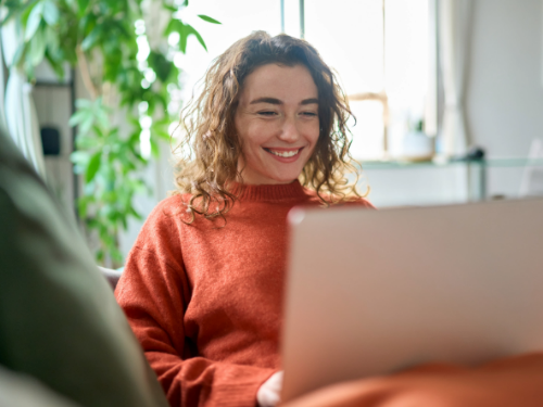 A person sat with a laptop on their lap smiling.