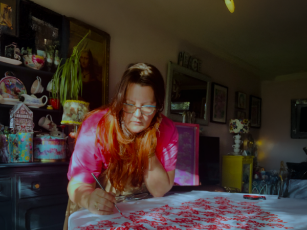 Student, Lorna Hall, stood at table in home working on art.