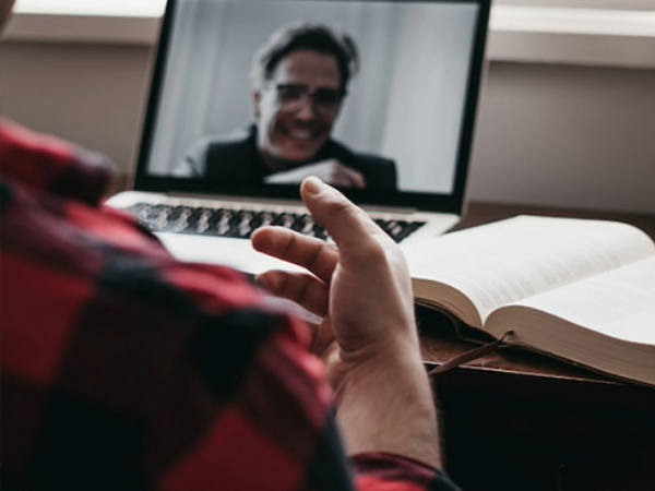 man sat at desk, talking on video call through laptop