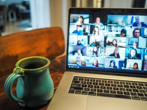 An image of a mug next to a laptop showing a Zoom conference call with many peoples webcams open showcasing their faces.