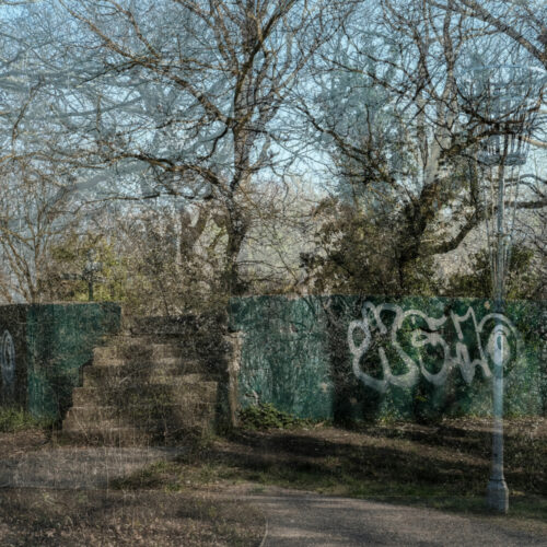 An image of a park area with trees and lamposts, featuring a wall with grafitti art on it.